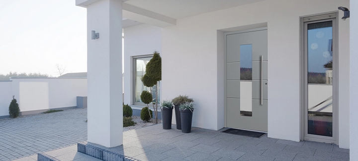 Moderner Hauseingang mit grauer Haustür und dekorativen Pflanzen.