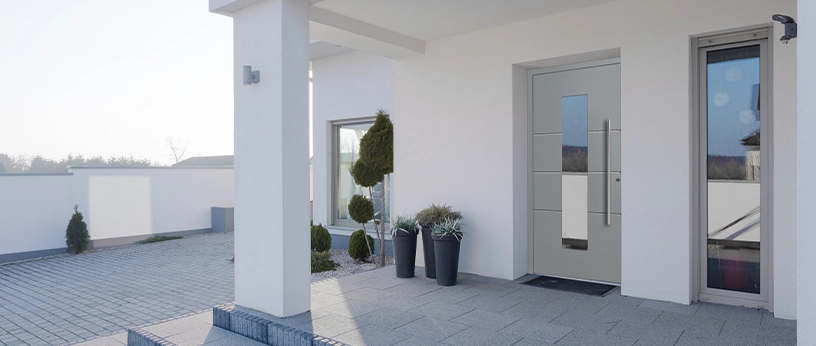 Moderner Hauseingang mit grauer Haustür und dekorativen Pflanzen.