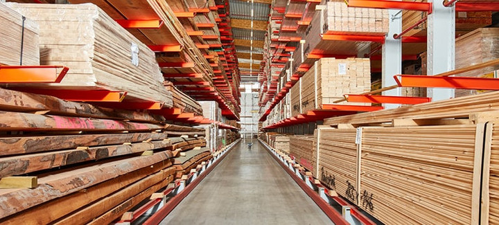 Großes Holzlager mit gestapeltem Schnittholz, Kanthölzern und Brettern in hohen Regalen mit roten Trägern.