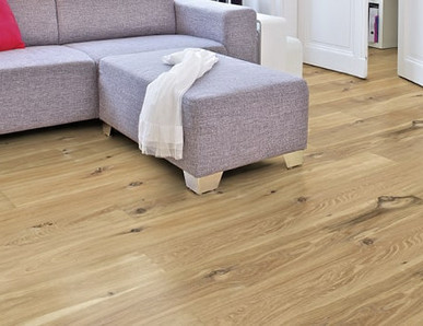 Im Wohnzimmer ist Parkett in Langdielen-Optik verlegt. Dazu passt ein Ecksofa mit bunten Kissen.