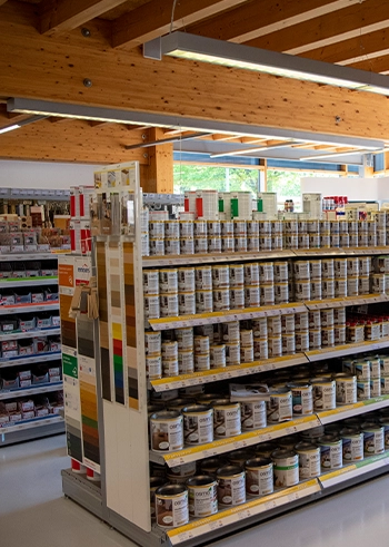 SB-Bereich bei Holz Langen mit Regalen voller Holzfarben und -öle sowie ausgestellten Holzmusterplatten.