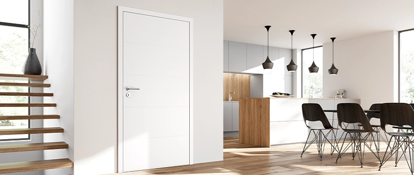 Helles, modernes Wohnambiente mit weißer Innentür, offener Küche und Essbereich mit schwarzen Stühlen.