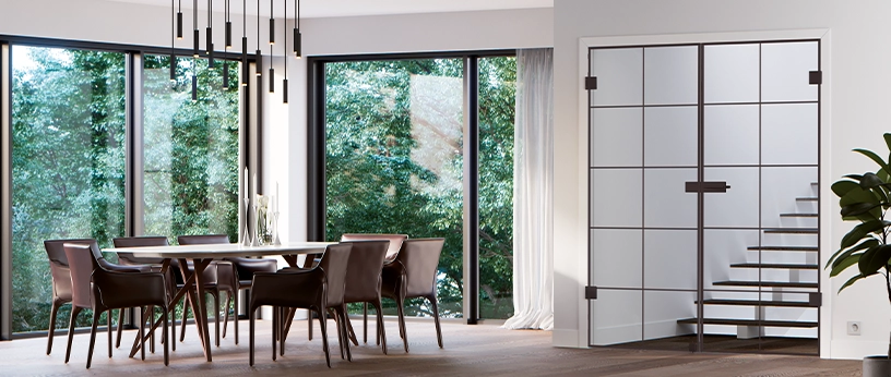 Schwarze Lofttür mit Sprossen als Raumtrenner neben großen Fenstern in einem modernen Essbereich.