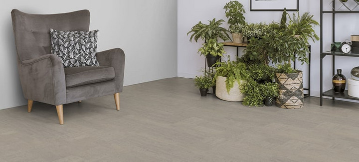 Der Boden im Wohnzimmer ist mit hellgrauem Kork belegt. Es gibt einen bequemen Sessel und einen Ständer mit Grünpflanzen.