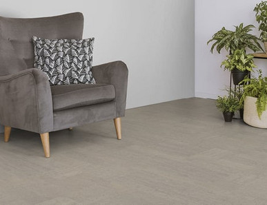 Der Boden im Wohnzimmer ist mit hellgrauem Kork belegt. Es gibt einen bequemen Sessel und einen Ständer mit Grünpflanzen.