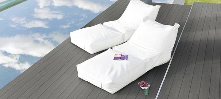 Graue WPC-Terrasse neben einem Pool mit zwei weißen Sonnenliegen.