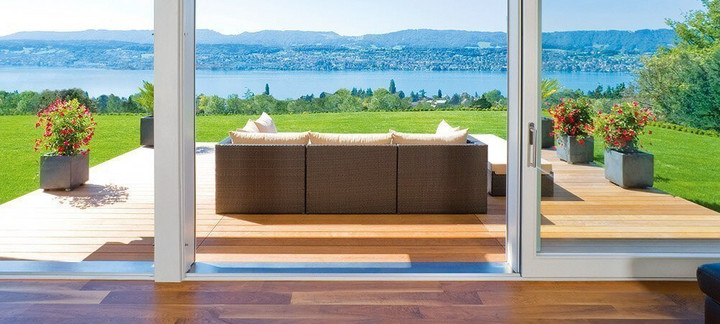 Holzterrasse mit Gartensofa, Topfpflanzen in der Ferne und Blick auf Fluss und Berge.