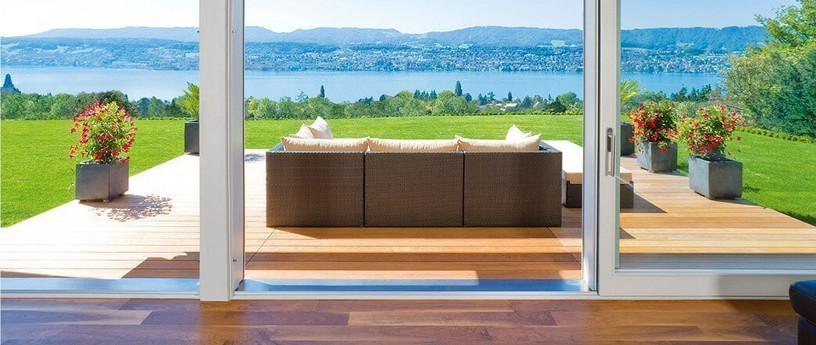 Holzterrasse mit Gartensofa, Topfpflanzen in der Ferne und Blick auf Fluss und Berge.