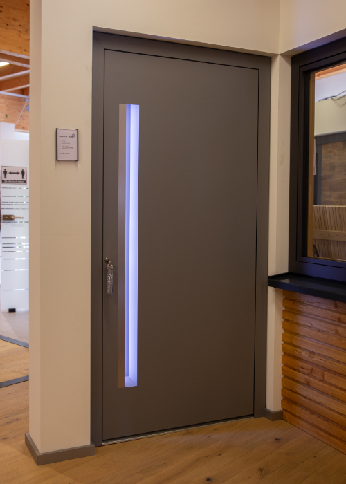 Graue Haustür mit schmalem vertikalem LED-beleuchtetem Glaseinsatz in der Türenausstellung von Holz Langen.